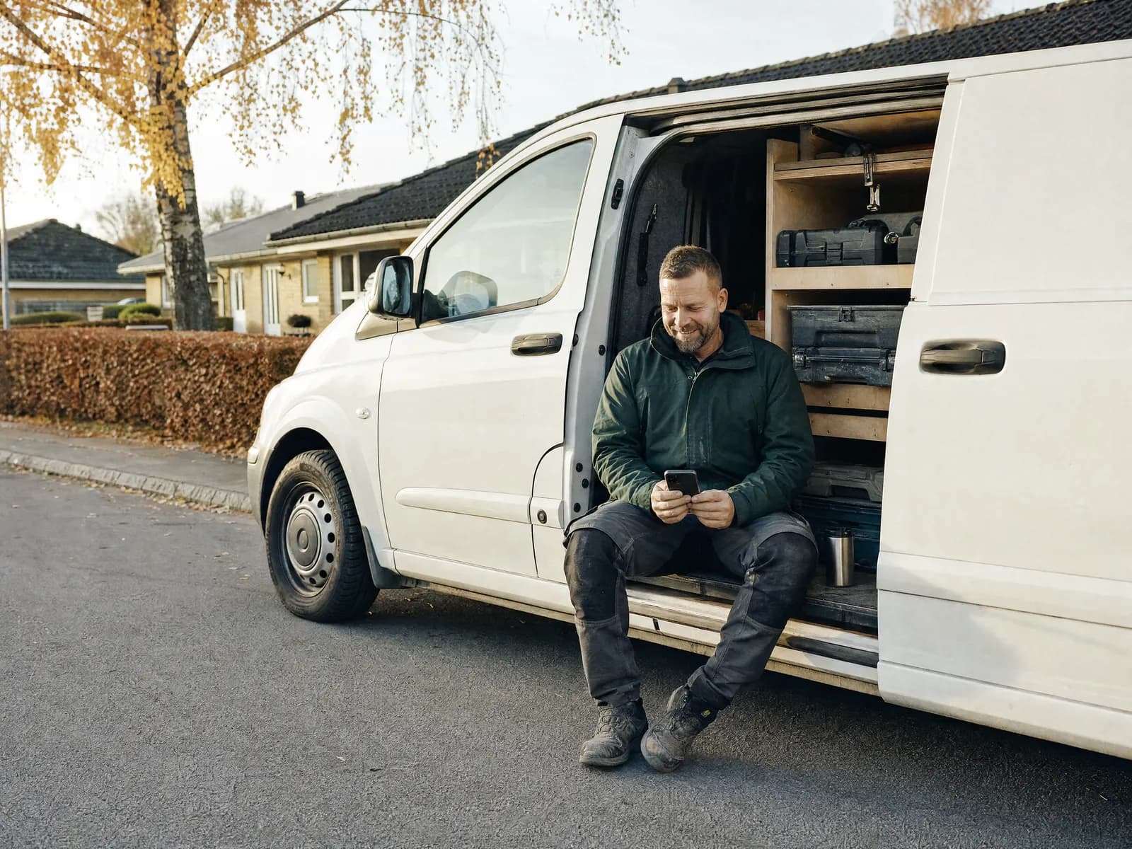 Illustration: håndværker sidder i sidedøren på sin varevogn på en villavej og læser resuméerne på telefonen